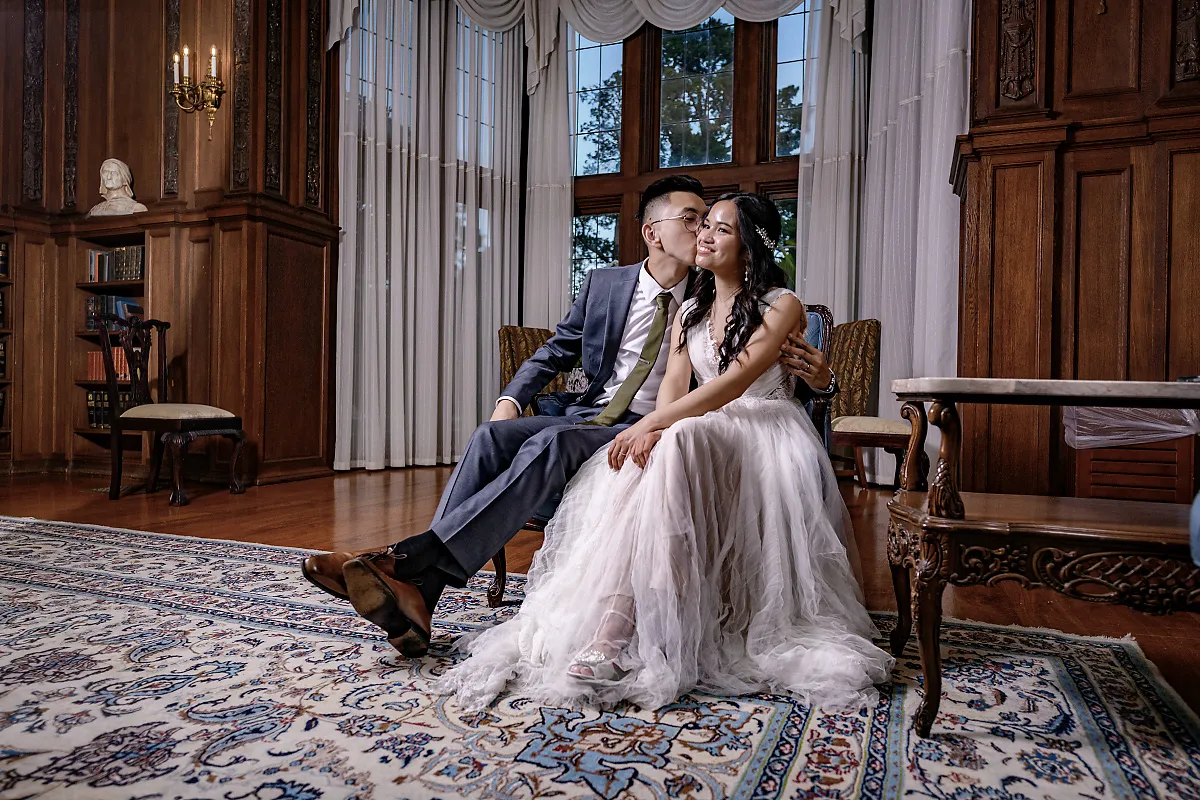 Bride and groom sharing a kiss on the cheek in an elegant wood-paneled room