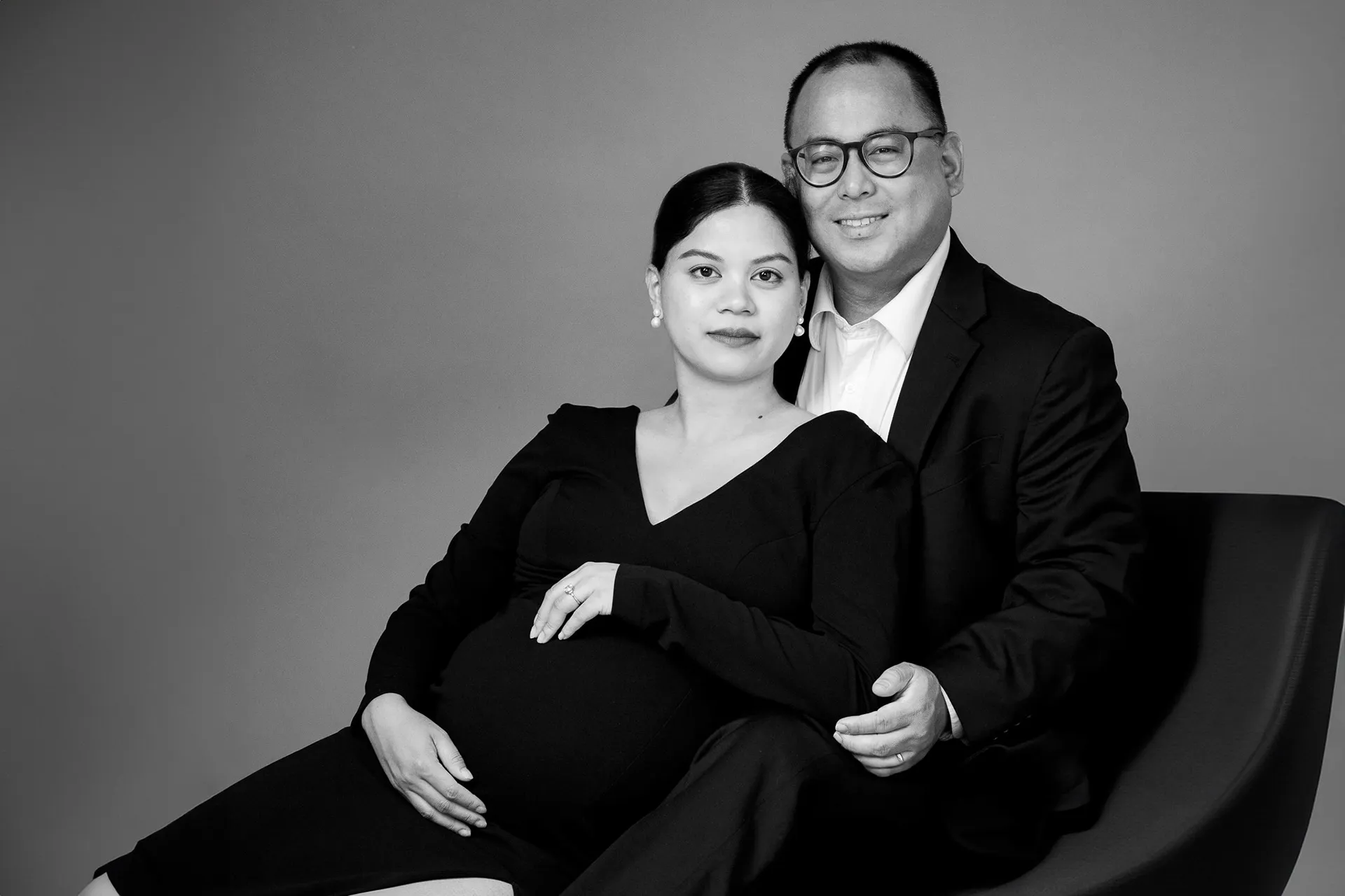 Black and white maternity portrait of an expecting couple together on a lounge chair