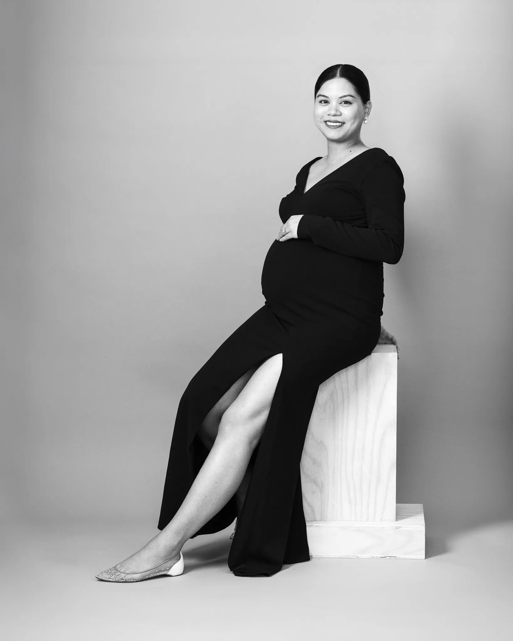 Black and white maternity portrait of a pregnant woman seated with hand on her belly