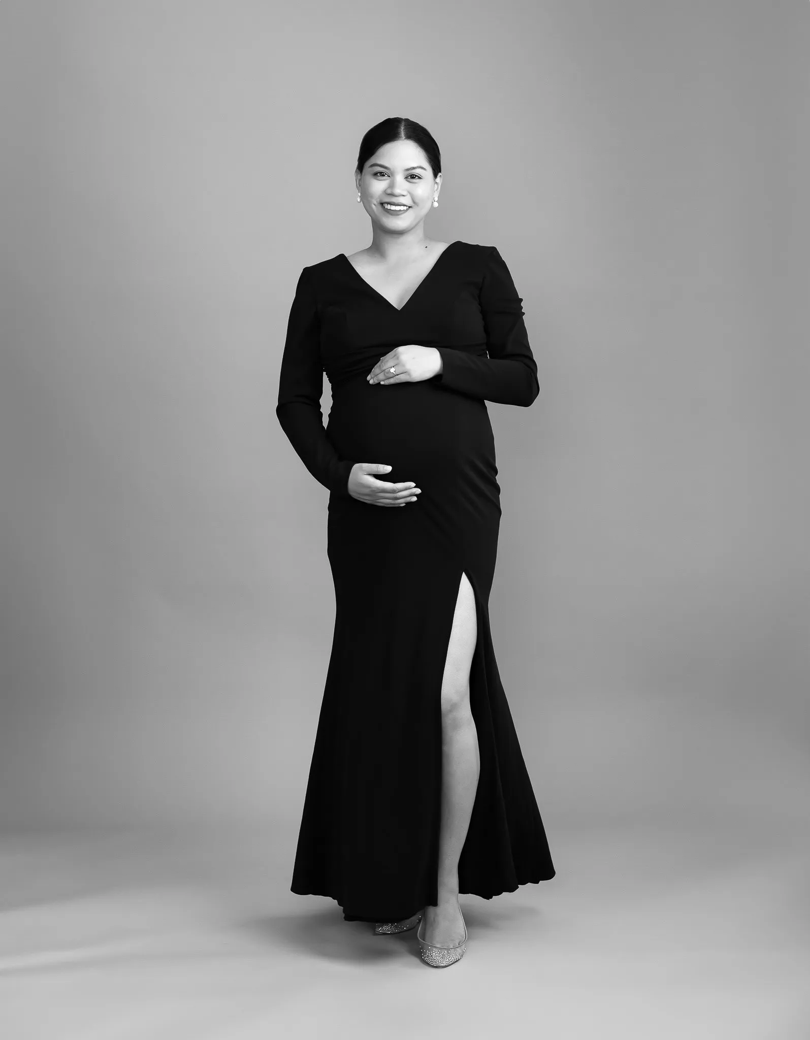 Black and white maternity portrait of a pregnant woman standing with hand on her belly