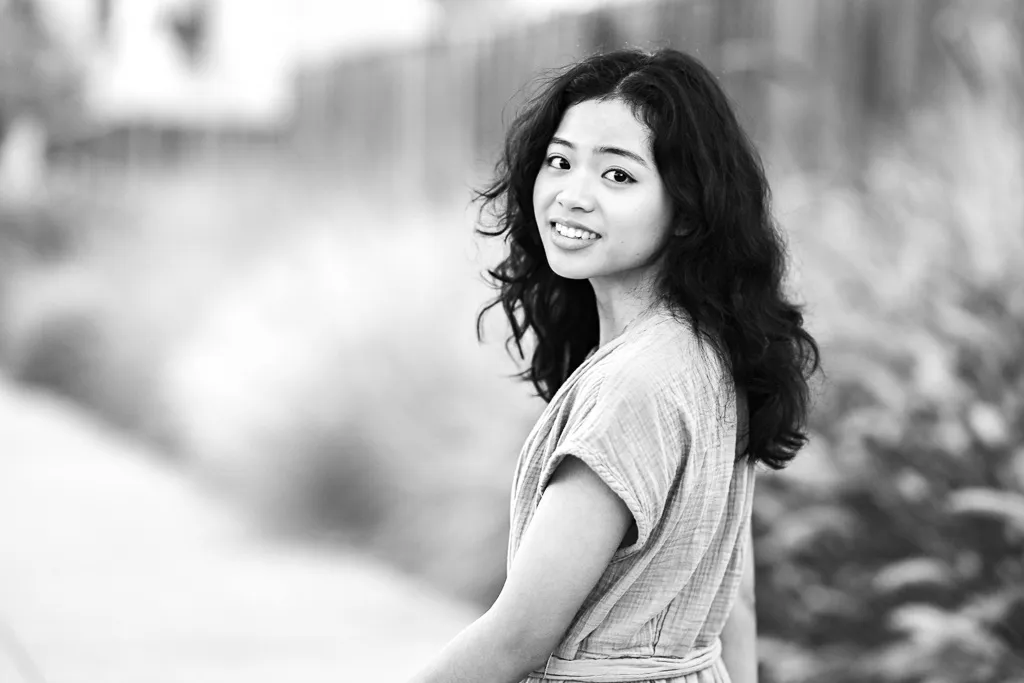 Black and white portrait of a young woman looking back over her shoulder outdoors