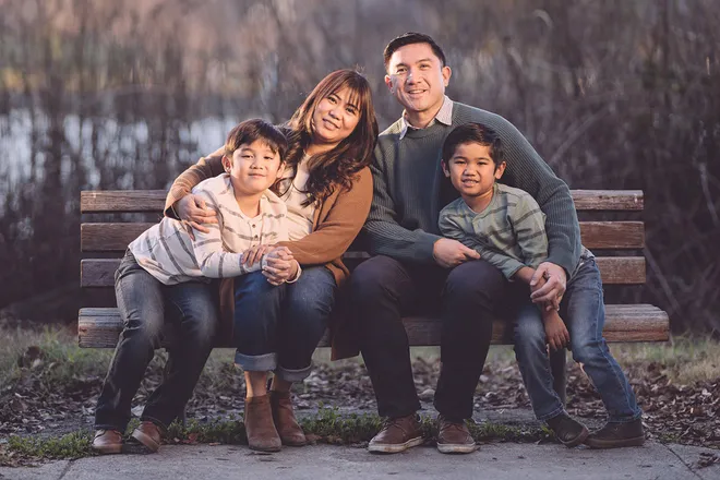 Family with two young sons seated together on a park bench