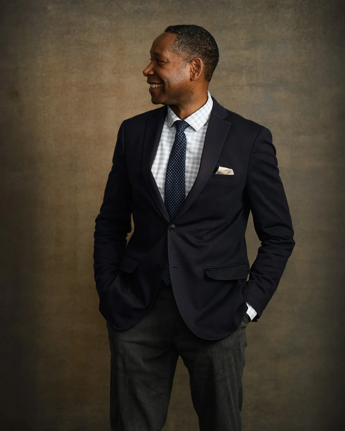 Man in a navy blazer smiling and looking off camera for a studio portrait