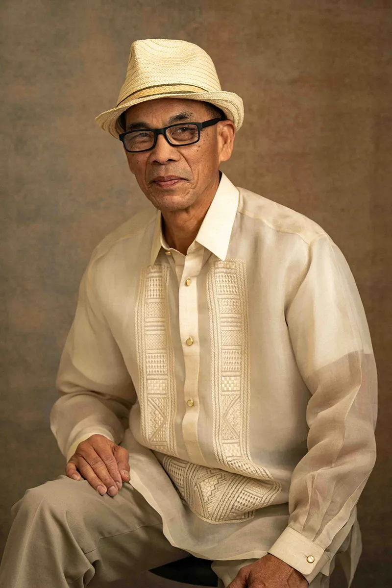 Older man in a straw hat and traditional barong seated for a studio portrait