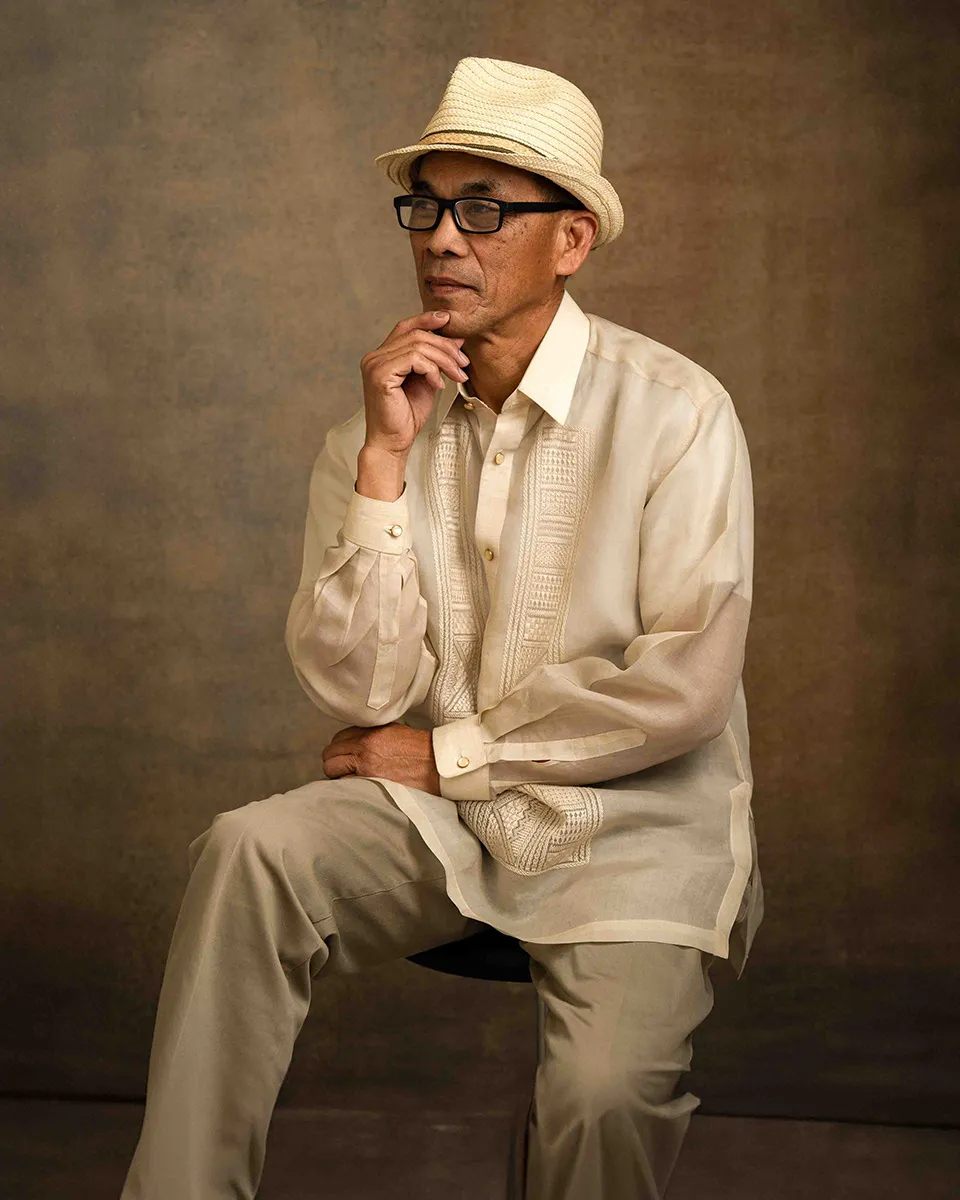 Older man in a straw hat and traditional barong resting chin on hand