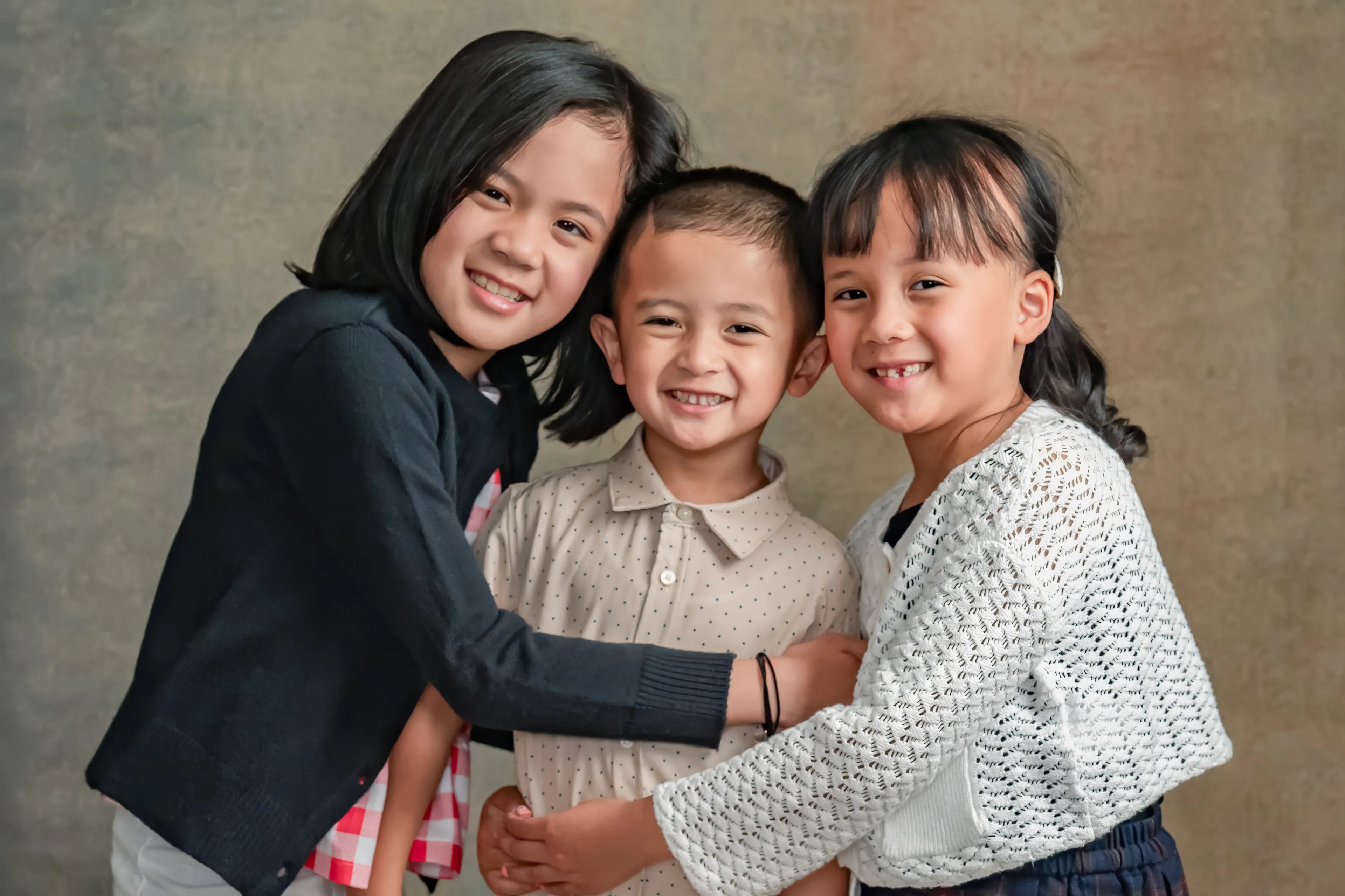 Three siblings embracing together in a studio portrait