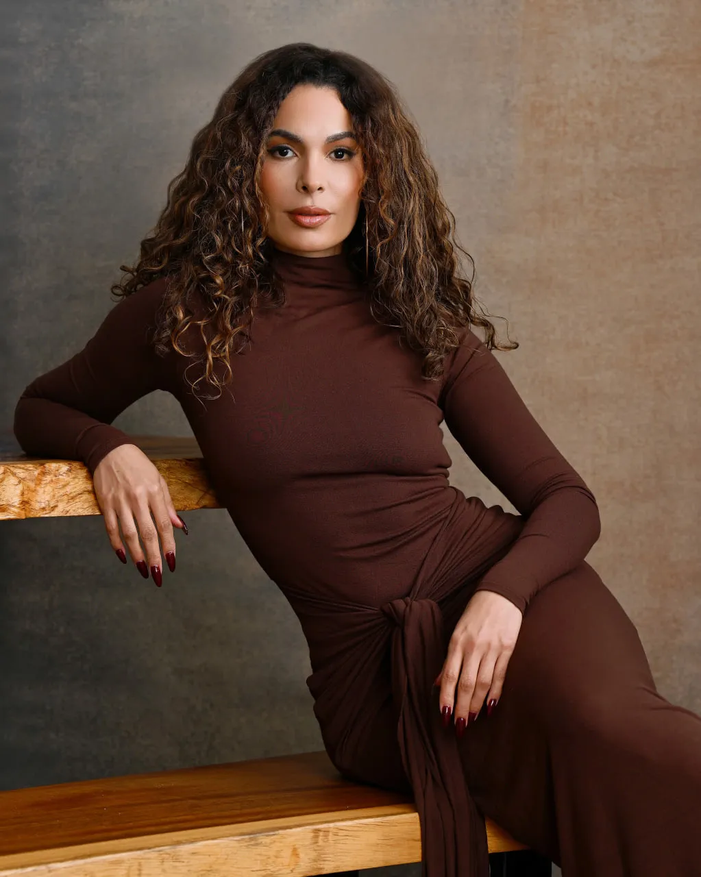 Woman with curly hair leaning on a wood bench for a studio portrait