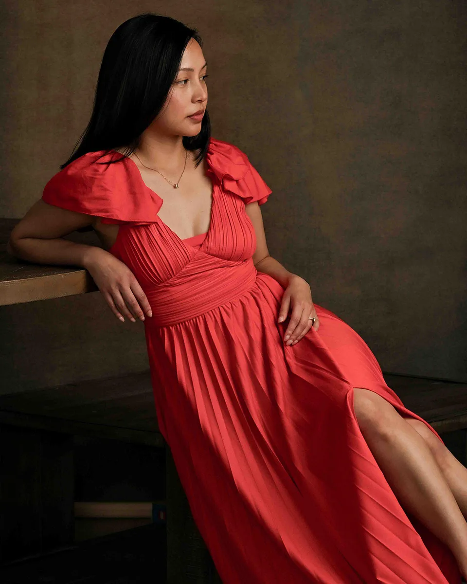 Woman in a red dress leaning against a table for a studio portrait
