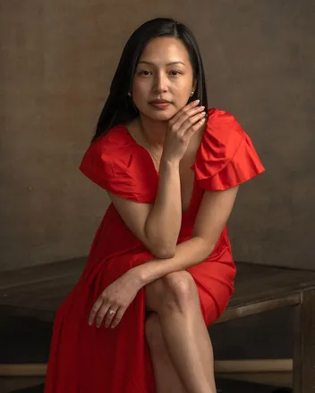 Woman in a red dress seated on a wood table for a studio portrait